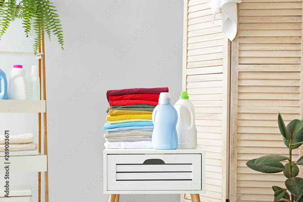 Stack of clean laundry and washing agents on table in bathroom