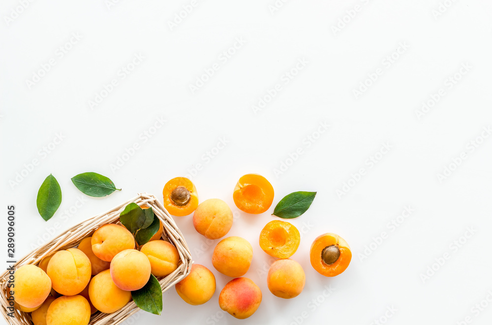 Fresh raw apricots in basket on white background top view copy space, pattern with leaves