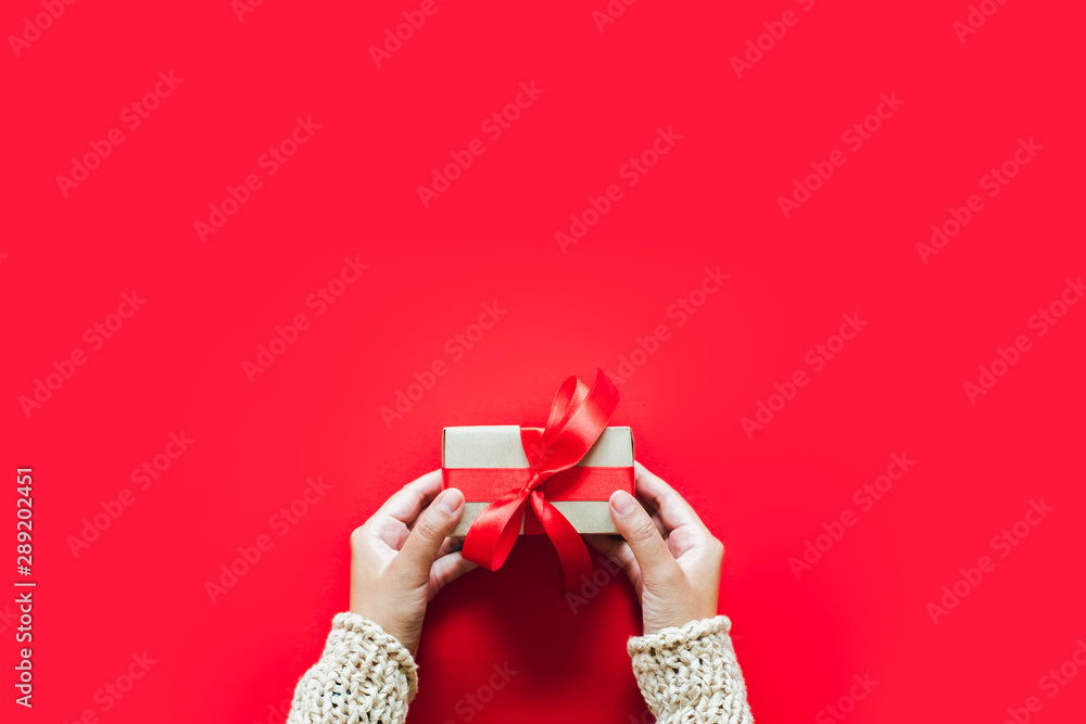 Hand holding gift/presents box over red background for chirstmas and happy new year concept. topview