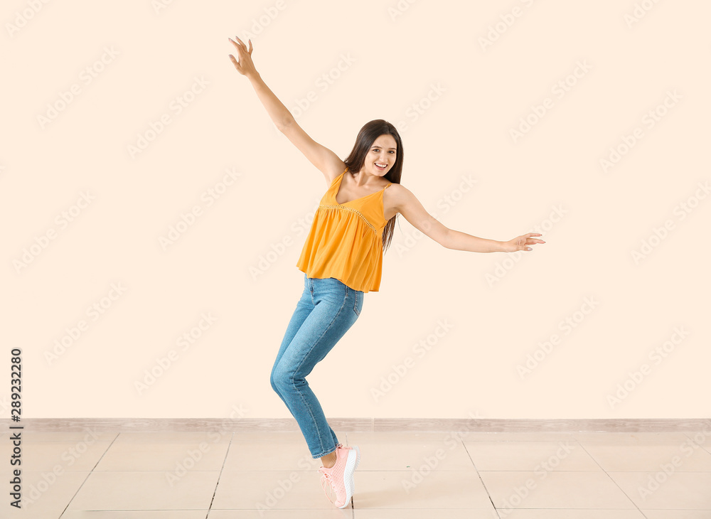 Dancing young woman against light wall