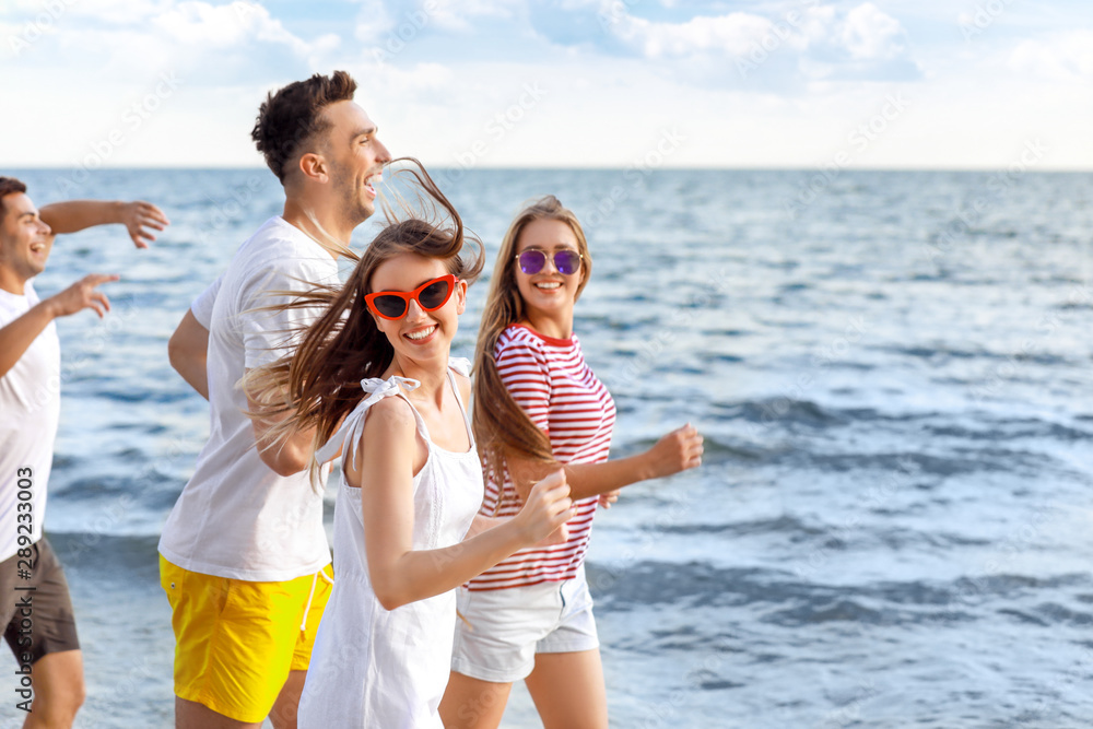 Happy friends running on sea beach at resort