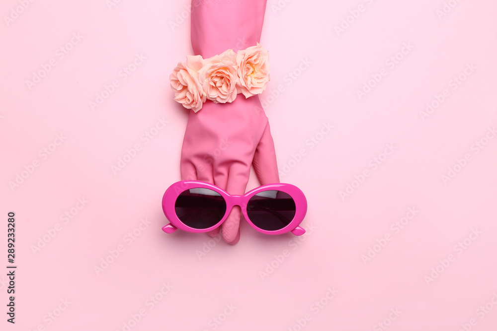 Stylish sunglasses with rubber glove and flowers on color background