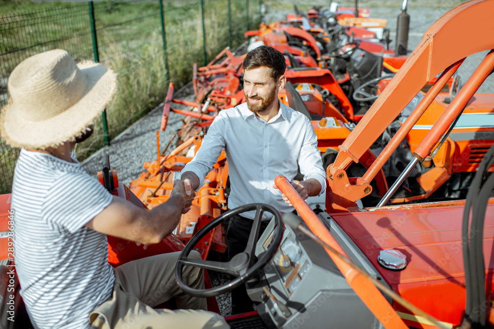 Young agronomist with elegant salesman choosing a tractor for farming on the open ground of agricult