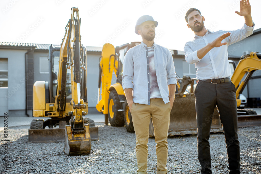 Builder choosing heavy machinery for construction with a sales consultant on the open ground of a sh