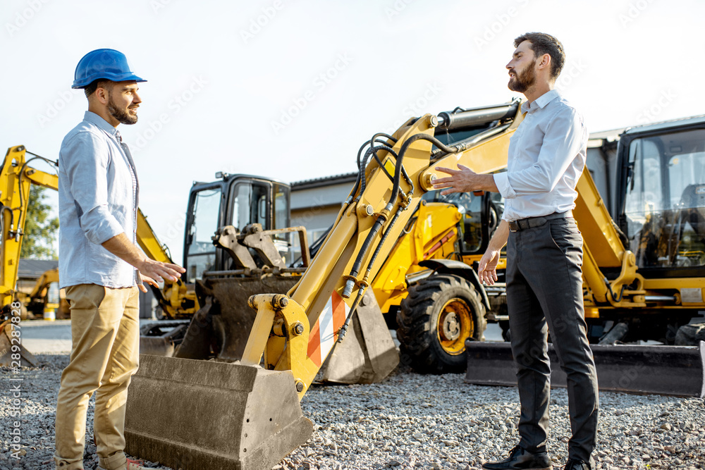 Builder choosing heavy machinery for construction with a sales consultant on the open ground of a sh