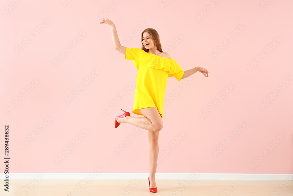 Beautiful young woman dancing against color wall