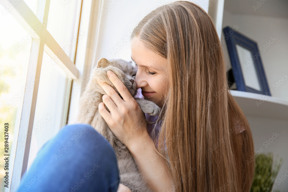 Beautiful woman with cute cat sitting near window