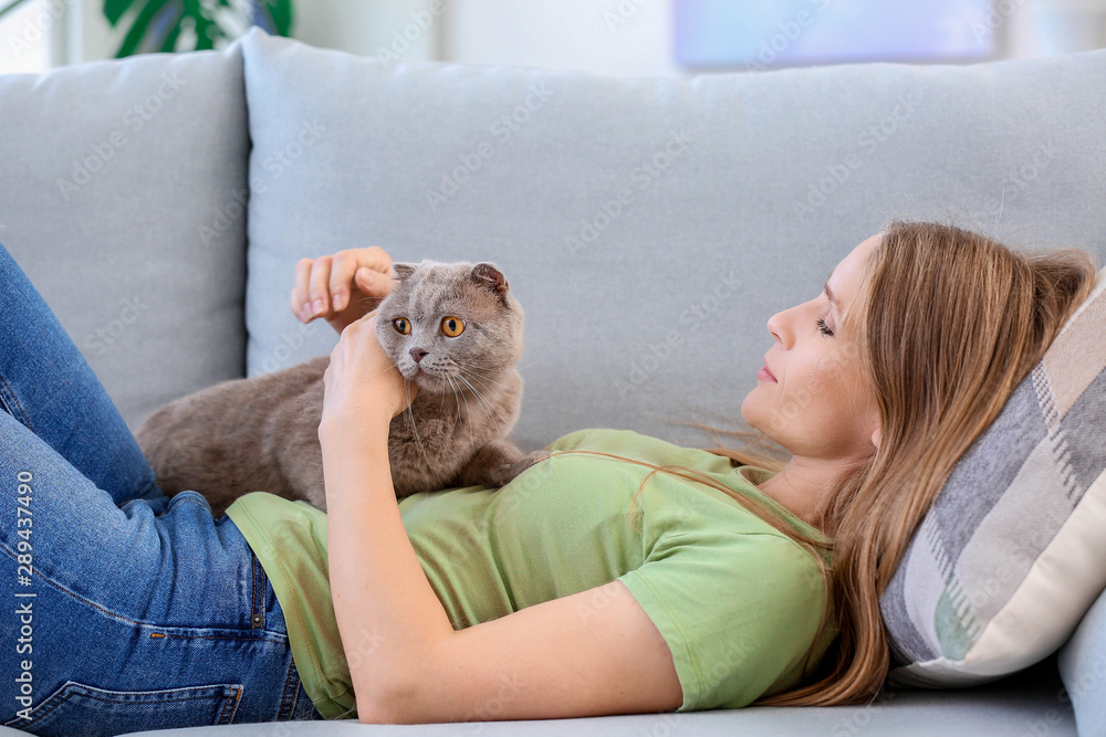 美丽的女人和可爱的猫躺在家里的沙发上