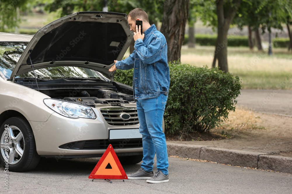 Man calling his insurance agent while standing near broken car on road