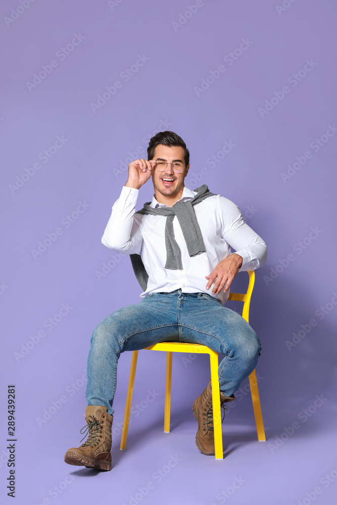 Fashionable man sitting on chair against color background