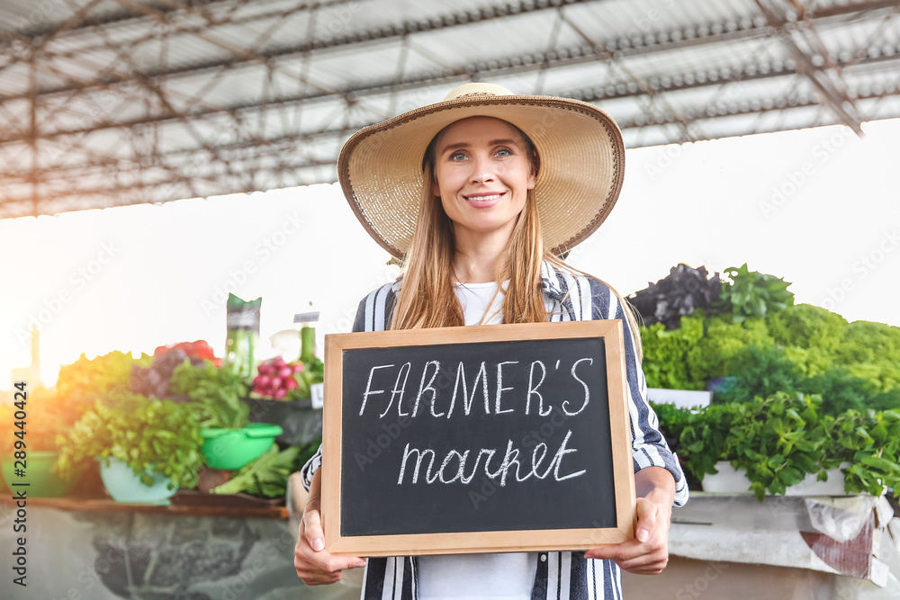 Woman holding chalkboard with text FARMERS MARKET outdoors