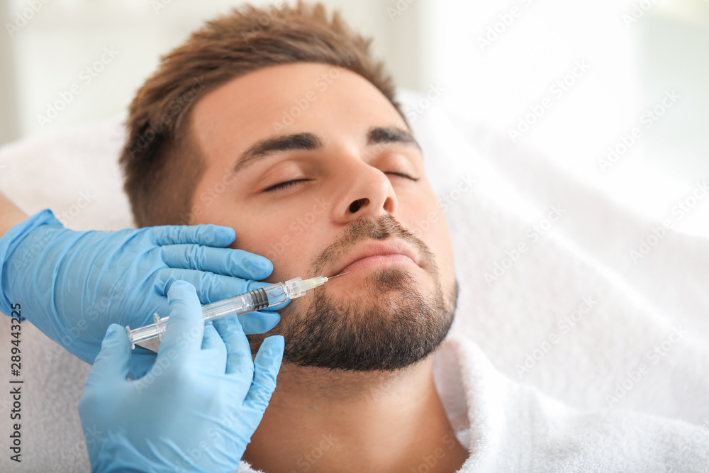 Handsome man receiving filler injection in beauty salon