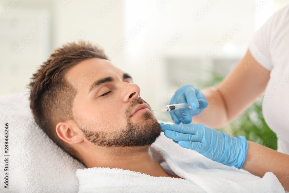 Handsome man receiving filler injection in beauty salon