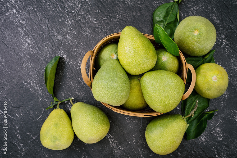 Fresh pomelo, pummelo, grapefruit, shaddock in bamboo basket with leaf on dark black slate backgroun