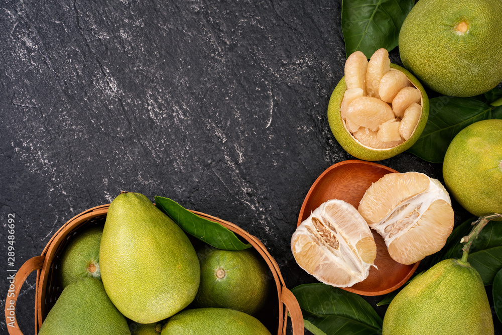 Fresh pomelo, pummelo, grapefruit, shaddock in bamboo basket with leaf on dark black slate backgroun