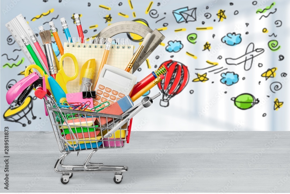 Variety office supplies in little shopping cart on wooden table  on background