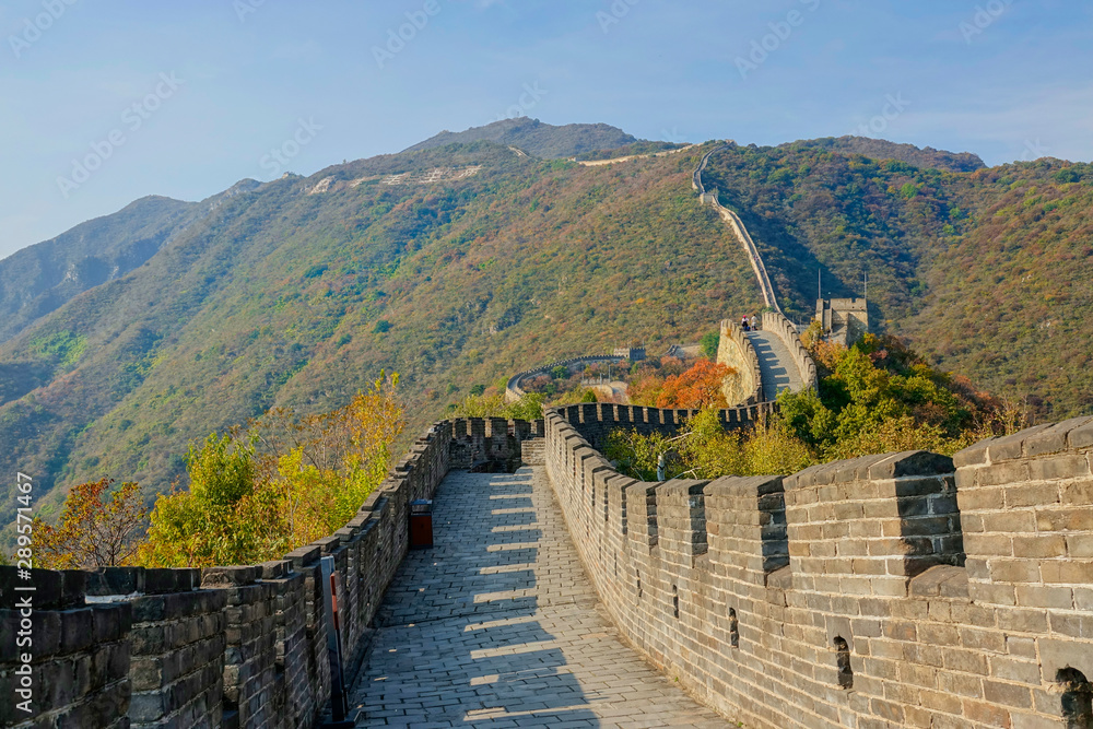 Travelers walk down walkway on top of famous Great Wall of China on sunny day