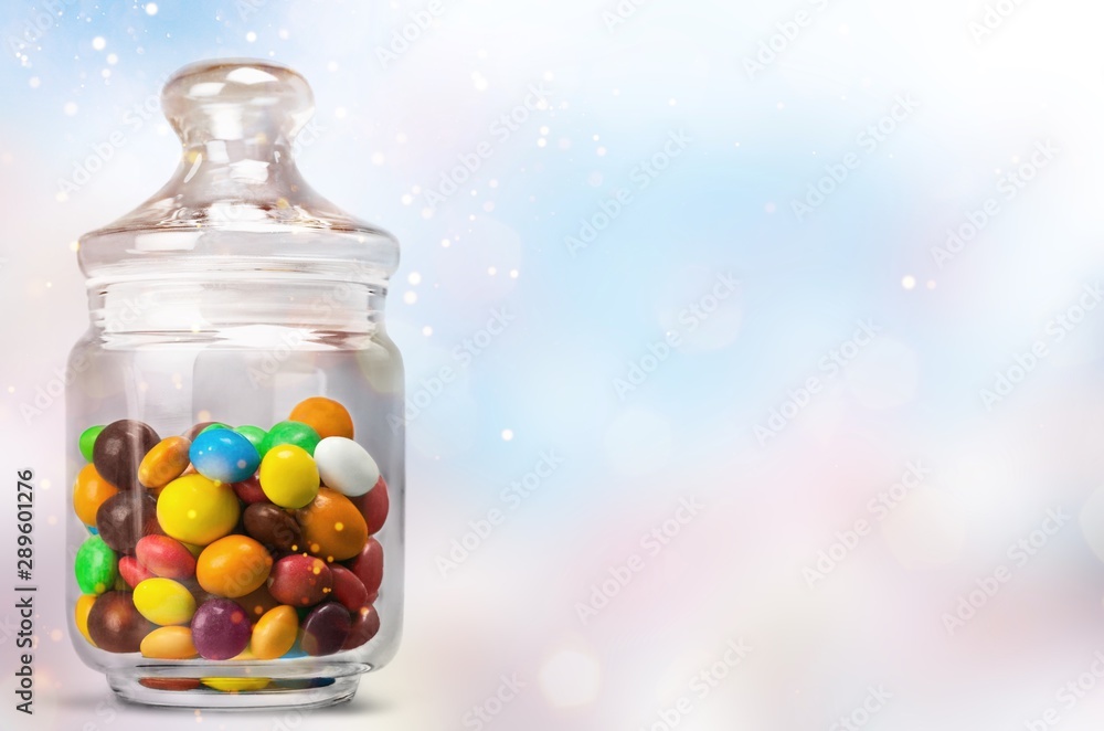 Transparent glass jar with colorful chocolate candies on table