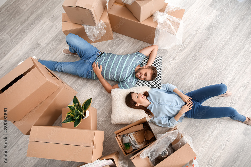 Happy young couple with belongings lying on floor in their new house