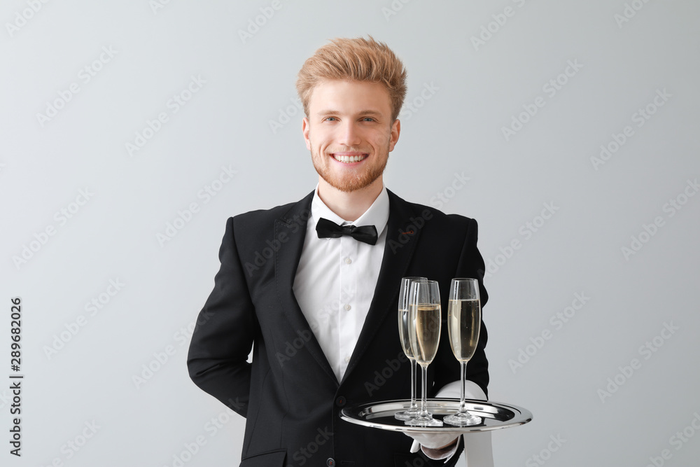 Handsome waiter with champagne on light background