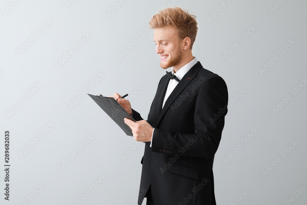 Handsome waiter with clipboard on light background