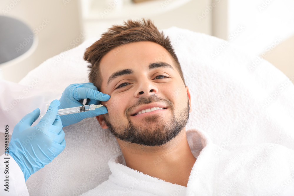 Handsome man receiving filler injection in beauty salon