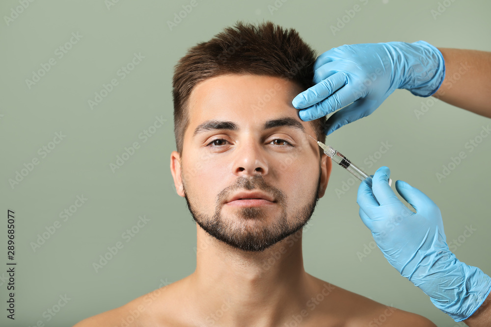 Handsome man receiving filler injection on color background