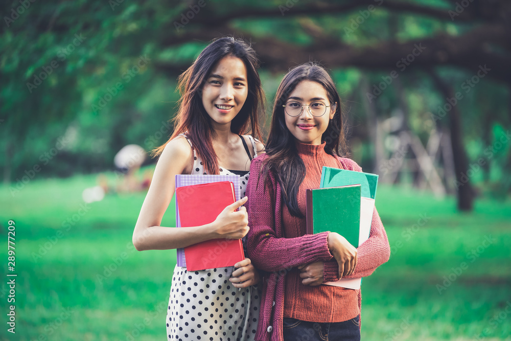 年轻的女学生朋友站在大学公园里手里拿着书。教育总结