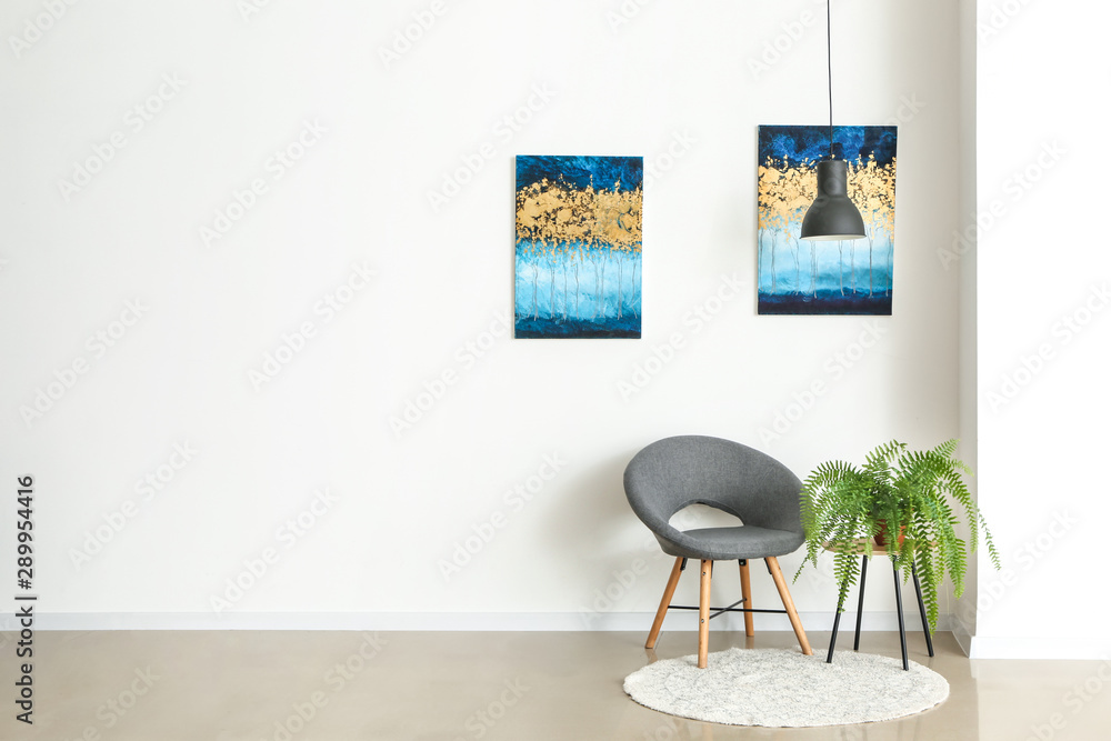 Chair and houseplant near light wall with pictures