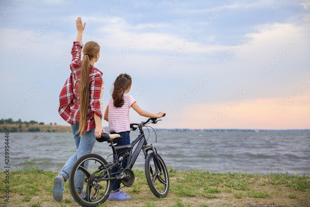 Woman and her little daughter with bicycle near river