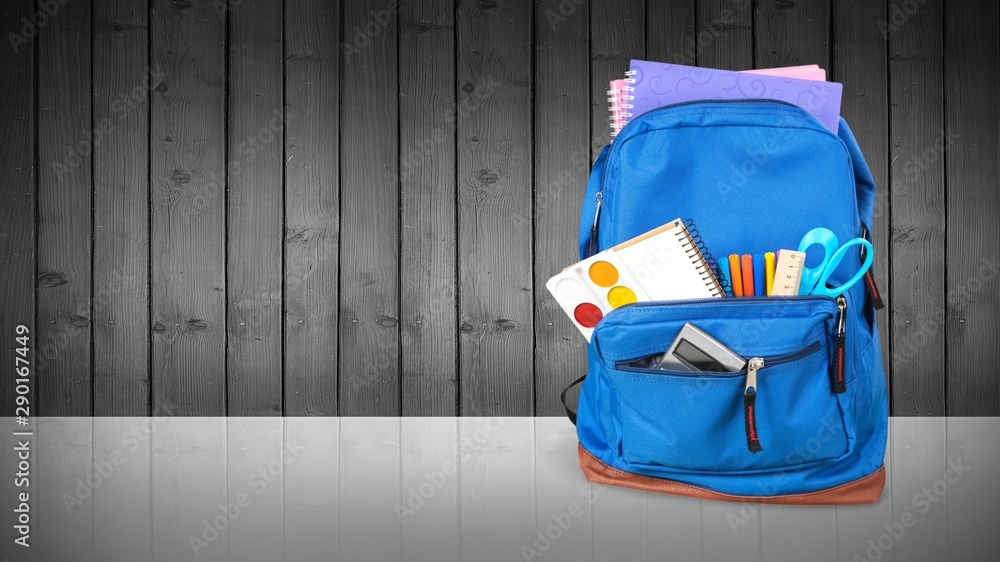 Colorful school supplies in backpack on wooden background