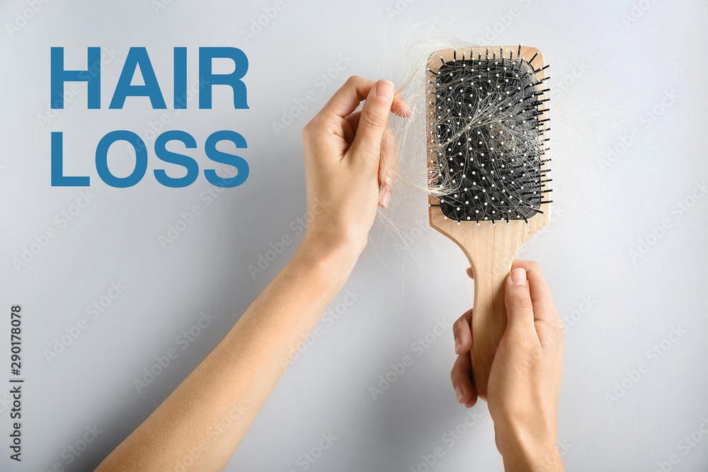 Female hands holding brush with fallen out hair on light background