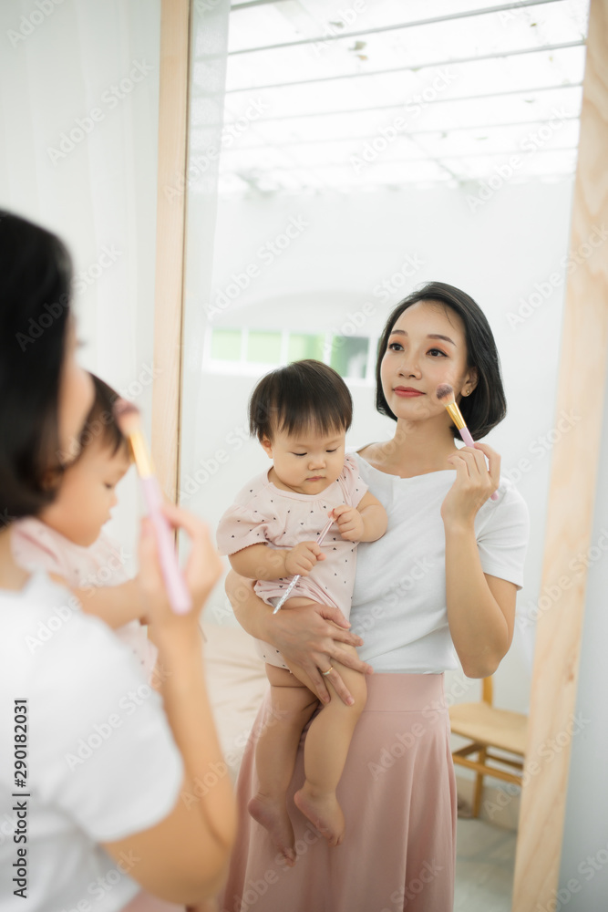 家里有个有趣的家庭。妈妈和她的小女儿正在化妆，在镜子附近玩得很开心。巴