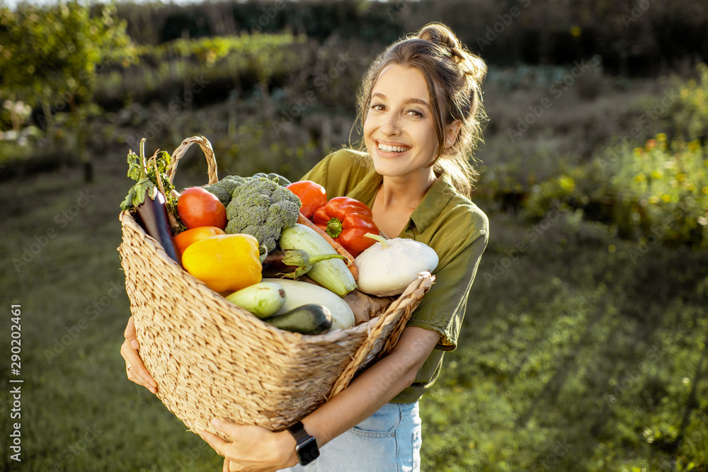 Portrait of a beautiful young woman with basket full of freshly picked up vegetables standing in the