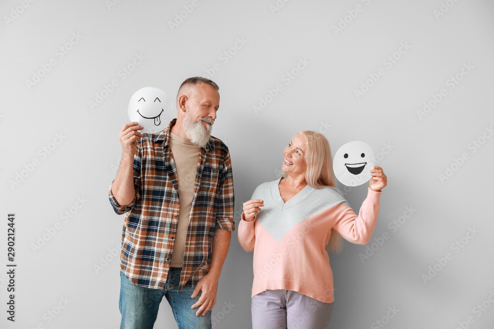 Happy mature couple with emoticons against light background