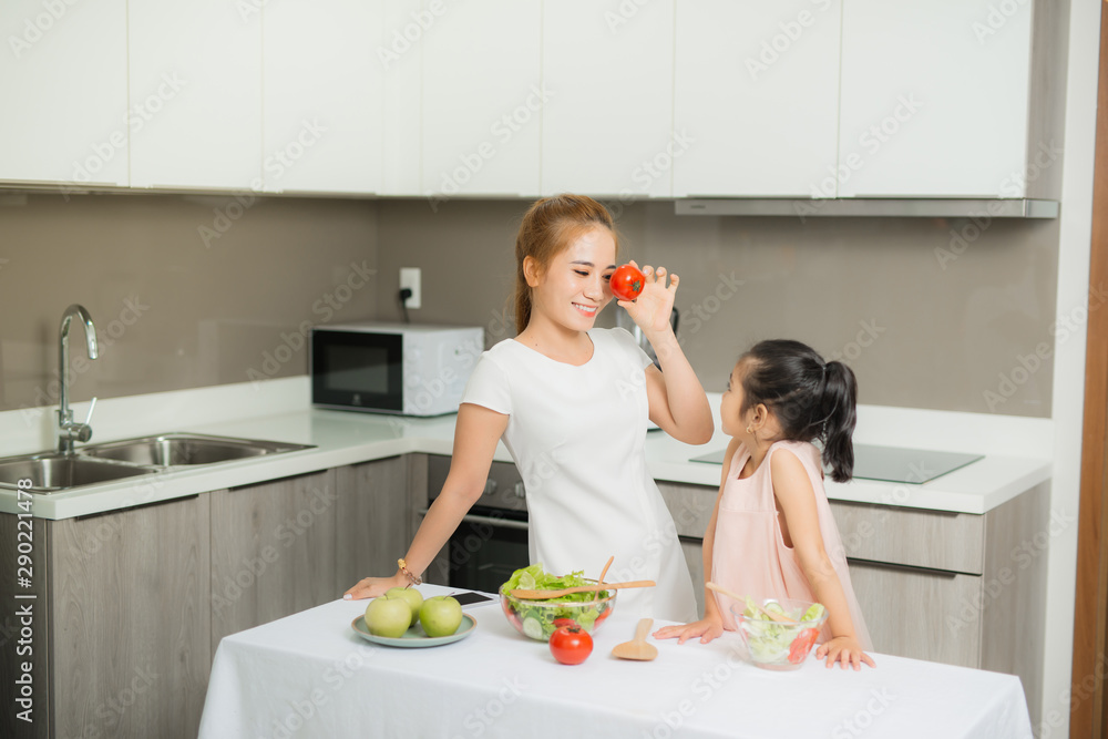 Cute little girl and her mom in chefs hats are cutting vegetables cooking a salad and smiling