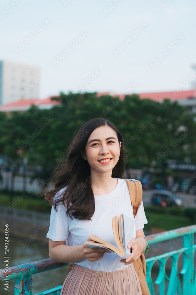 美丽的越南女孩站在风中看书的肖像，城市背景模糊。