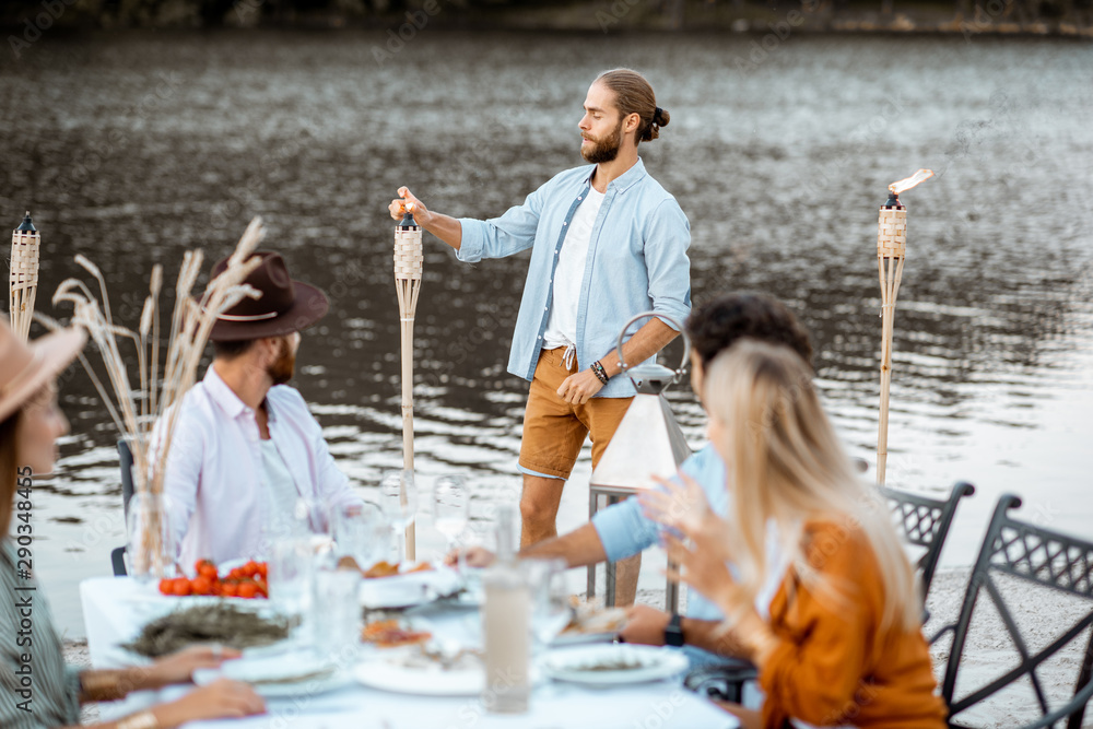 Group of young friends preparing for a festive dinner at the beautifully decorated table, man lighti