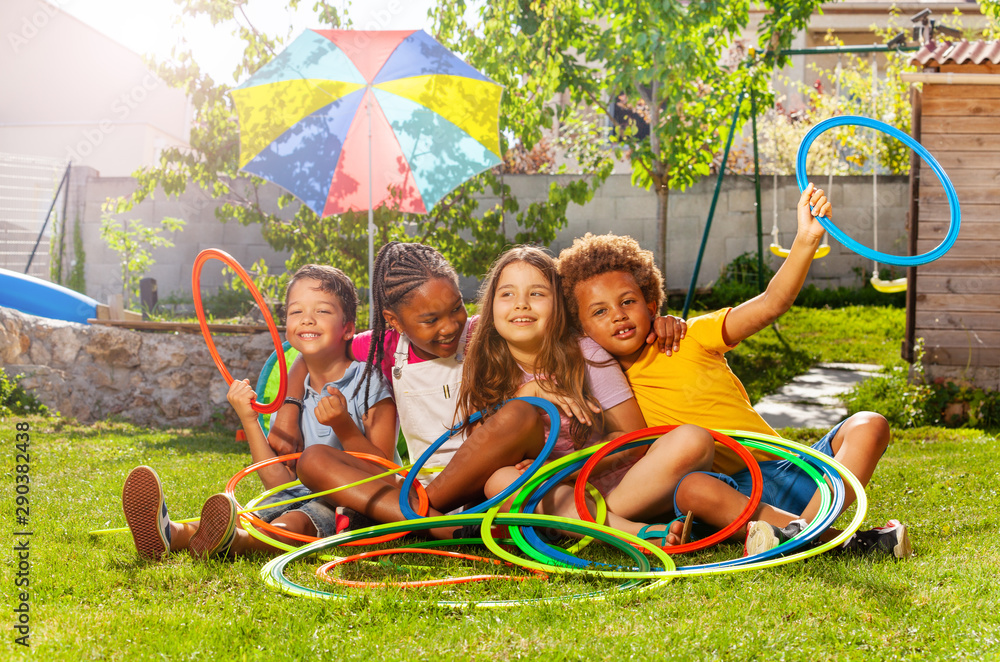 Four kids in a group sit with hula hoops on lawn