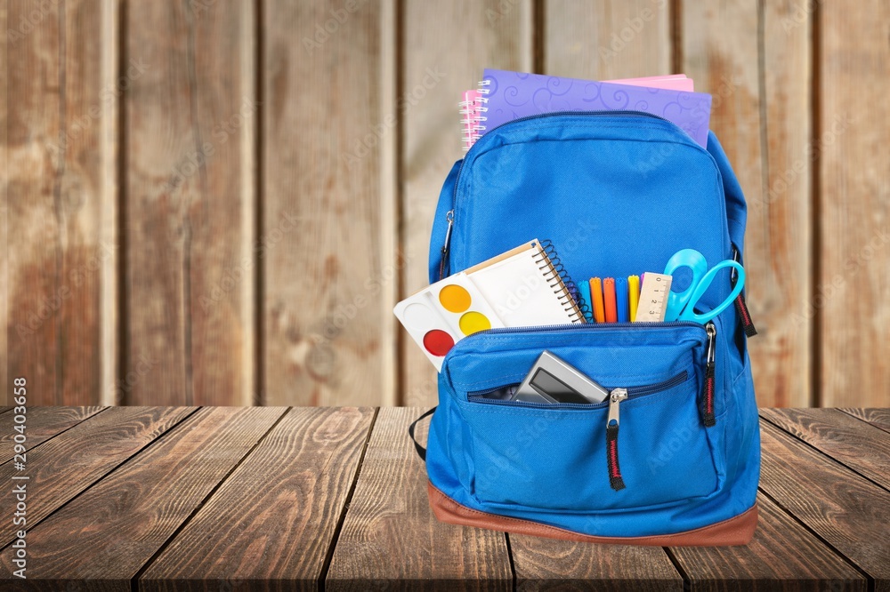 School Backpack with supplies on wooden background