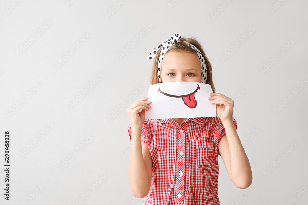 Little girl hiding mouth behind drawn smile on light background