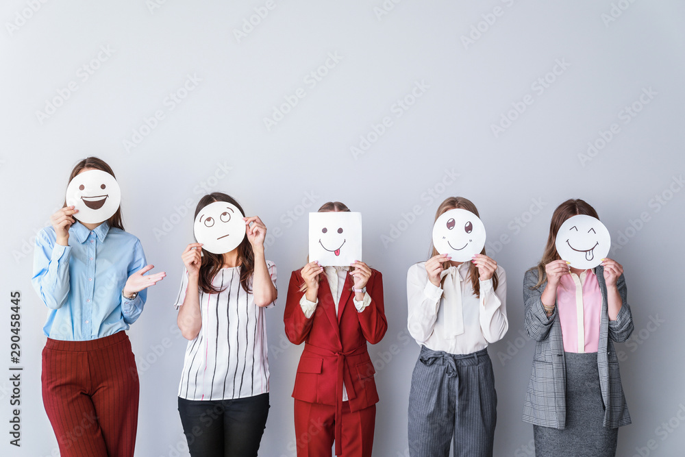 Group of woman covering their faces with drawn emoticons against light background