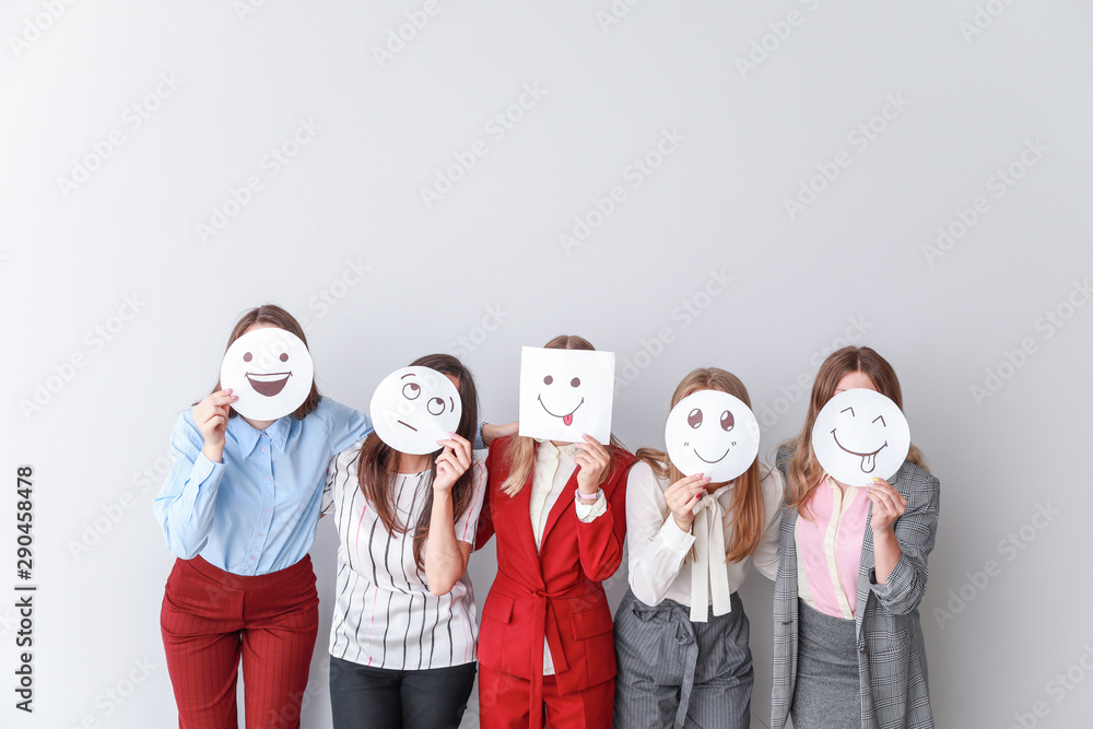 Group of woman covering their faces with drawn emoticons against light background