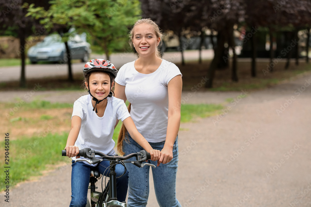 Mother teaching her daughter to ride bicycle outdoors