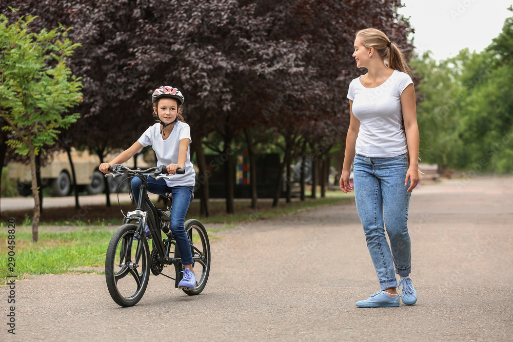 Mother teaching her daughter to ride bicycle outdoors