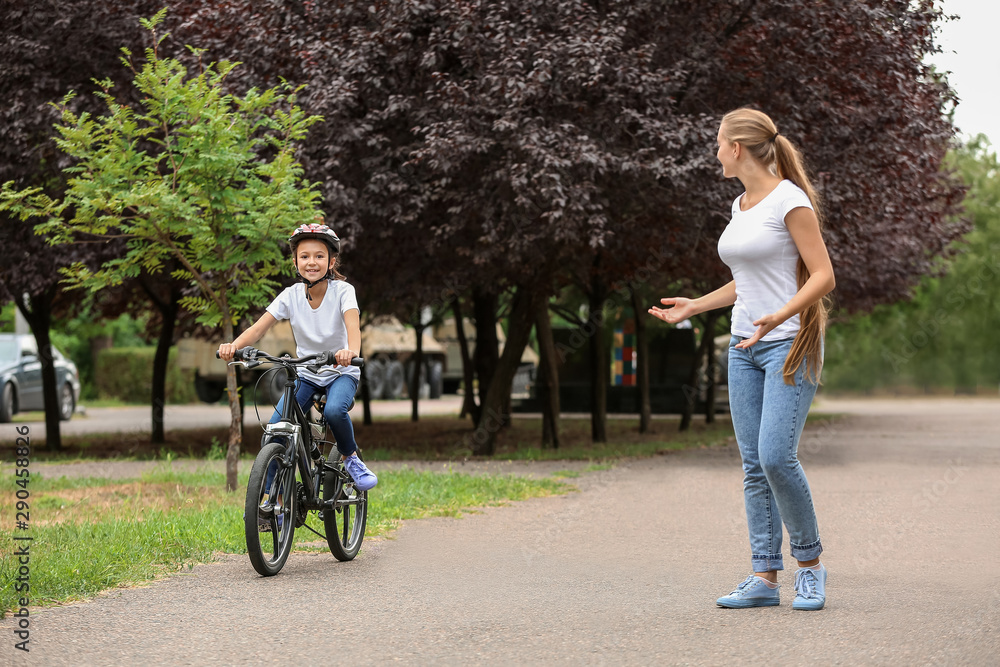 Mother teaching her daughter to ride bicycle outdoors