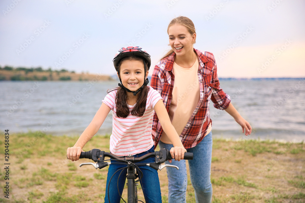 Mother teaching her daughter to ride bicycle outdoors