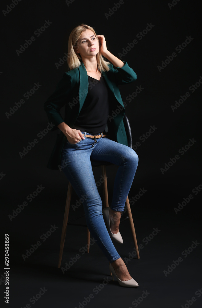 Beautiful stylish businesswoman sitting on chair against dark background