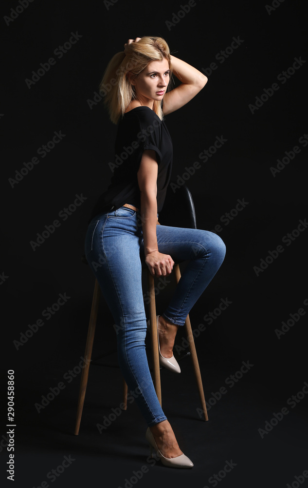 Beautiful stylish woman sitting on chair against dark background