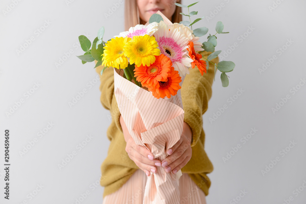 浅色背景上有一束美丽的非洲菊花的女人